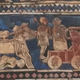 Two red chariots are pulled by teams of beige kungas in this ancient Mesopotamian artwork.